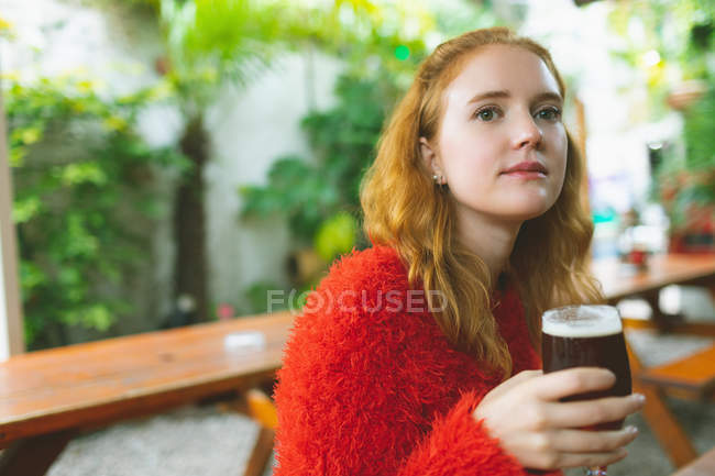 Redhead woman holding a glass of beer in outdoor cafe — Stock Photo