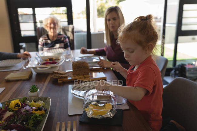 Chica apertura tapa de utensilio en mesa de comedor en casa - foto de stock