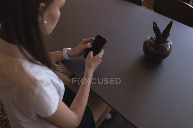 Жіночий керівник використовує мобільний телефон в кафетерії в офісі — стокове фото