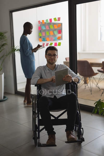 Виконавчий на інвалідному візку, дивлячись на камеру, використовуючи цифровий планшет в офісі — стокове фото