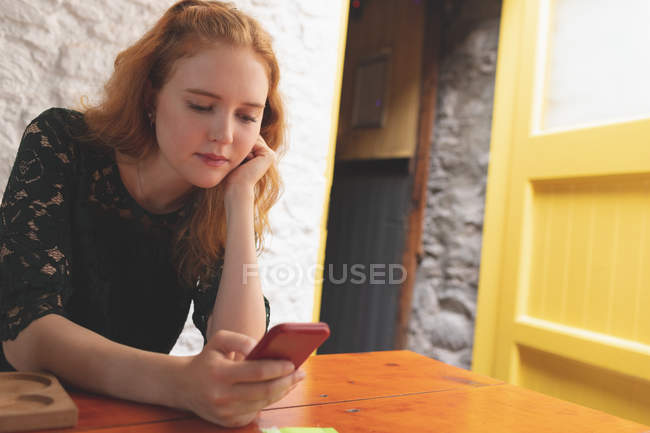Femme rousse utilisant un téléphone portable dans le café — Photo de stock
