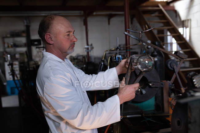 Vista lateral del trabajador masculino examinando el producto de vidrio en la fábrica de vidrio - foto de stock