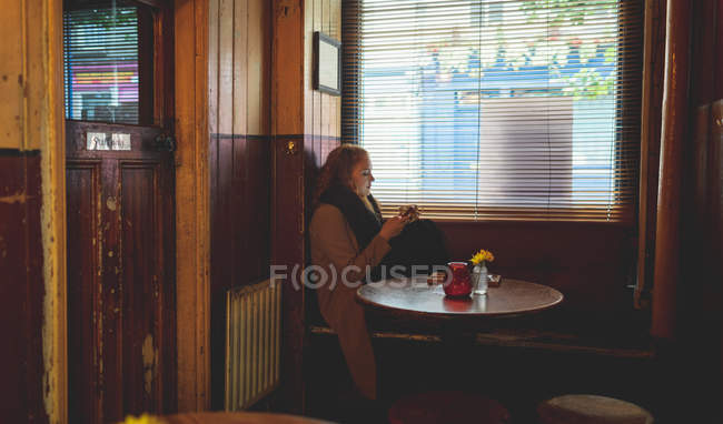 Mulher ruiva usando telefone celular enquanto toma café no café — Fotografia de Stock