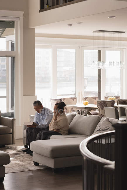 Старшая пара, использующая цифровой планшет и разговаривающая по мобильному телефону дома — стоковое фото