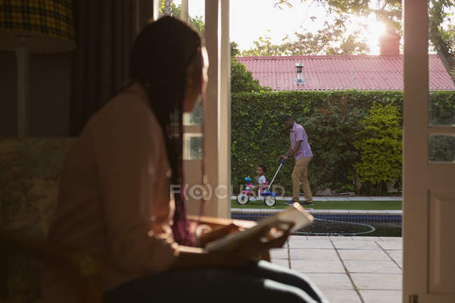 Father pushing son on tricycle while mother is looking out from home — Stock Photo