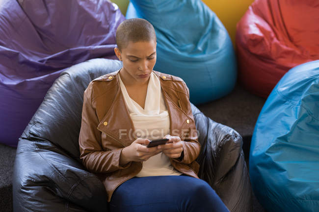 Керівник бізнесу, використовуючи мобільний телефон, сидячи на мішку для бобів в офісі — стокове фото