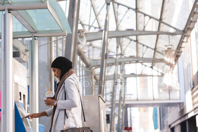 Вид сбоку женщины в хиджабе, пользующейся автоматом по продаже билетов на железнодорожном вокзале — стоковое фото