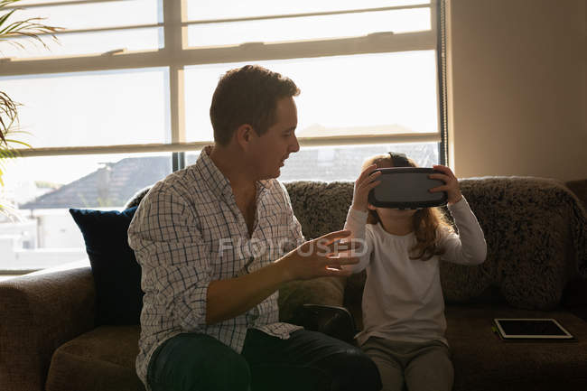 Girl using virtual reality headset with father in living room at home — Stock Photo