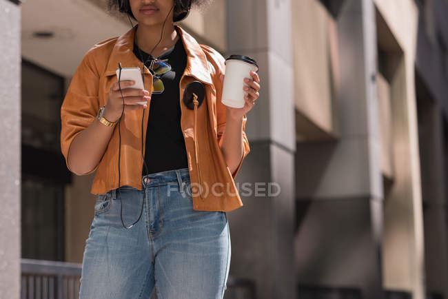 Mid section of woman having coffee while listening music on mobile phone — Stock Photo
