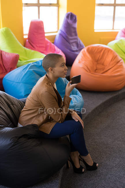 Female business executive talking on mobile phone while sitting on bean bag in office — Stock Photo
