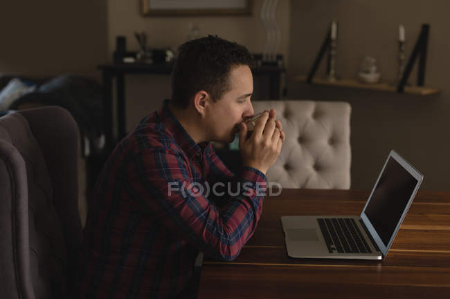 Man having coffee while using laptop in living room at home — Stock Photo