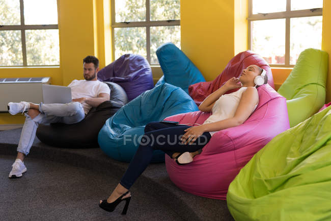 Führungskräfte entspannen sich und benutzen Laptop, während sie im Büro auf Sitzsäcken sitzen — Stockfoto