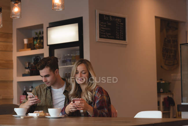 Молодая пара использует мобильный телефон в кафе — стоковое фото