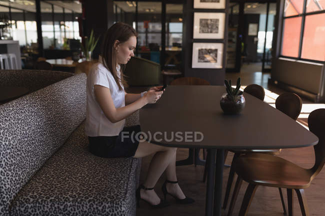 Жіночий керівник використовує мобільний телефон в кафетерії в офісі — стокове фото