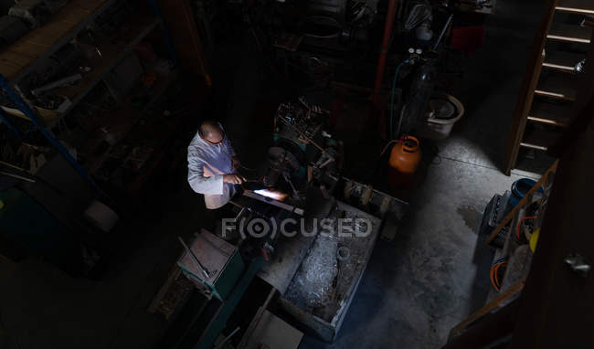Над чоловічим працівником використовуючи зварювальний факел на скляній фабриці — стокове фото