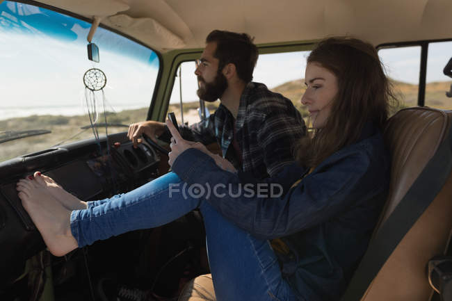 Woman using mobile phone while man driving car on roadtrip — Stock Photo