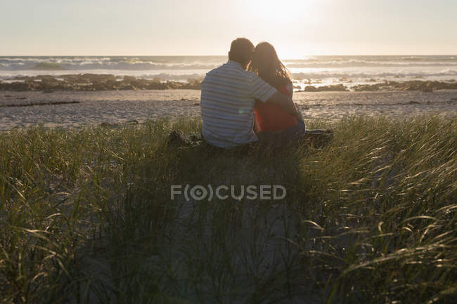 Вид сзади пары, сидящей на пляже во время заката — стоковое фото
