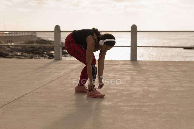 Женщина-инвалид, завязывающая шнурки на набережной возле моря — стоковое фото