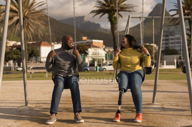 Couple heureux jouant sur la balançoire aire de jeux — Photo de stock