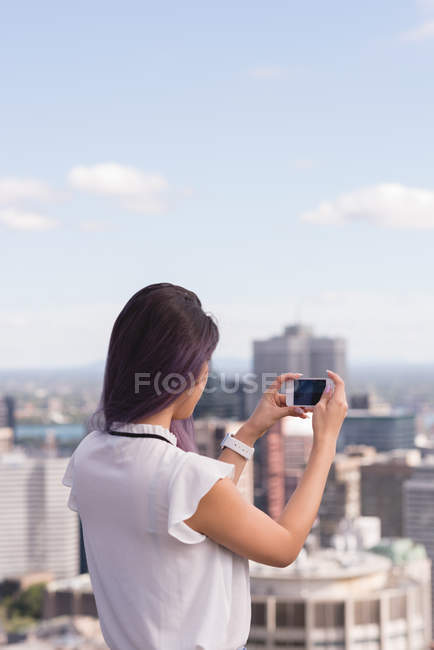 Vista trasera de la mujer haciendo clic en la foto en el teléfono móvil - foto de stock
