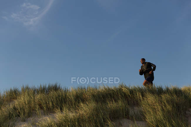 Atleta masculino trotando cerca de la playa en un día soleado - foto de stock