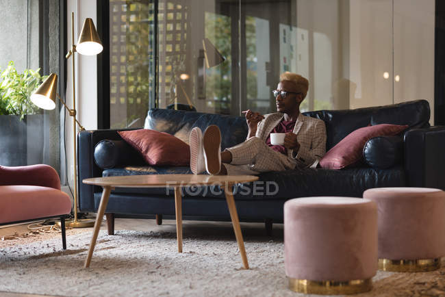 Empresário falando no celular enquanto toma café no escritório — Fotografia de Stock