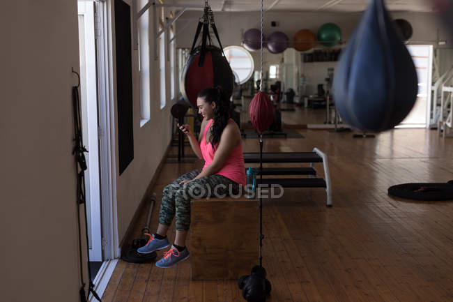 Vista lateral del boxeador femenino utilizando el teléfono móvil en el gimnasio - foto de stock