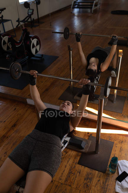 Boxeadora joven haciendo ejercicio con barra de pesas en gimnasio - foto de stock