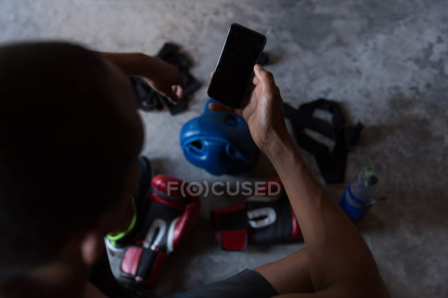 Vue grand angle du boxeur masculin en utilisant le téléphone portable dans le club de boxe — Photo de stock
