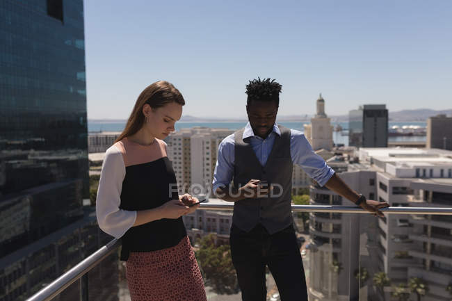 Бізнес-колеги використовують мобільний телефон на терасі в офісі — стокове фото
