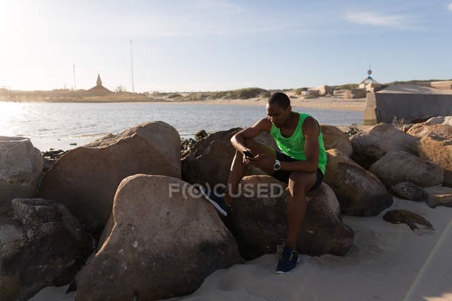 Athlète masculin utilisant un téléphone portable près de la plage par une journée ensoleillée — Photo de stock