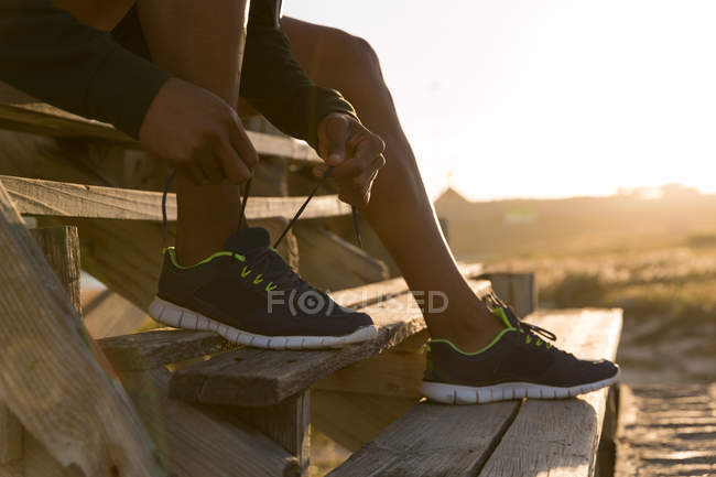 Крупный план спортсмена, завязывающего шнурки на пирсе — стоковое фото