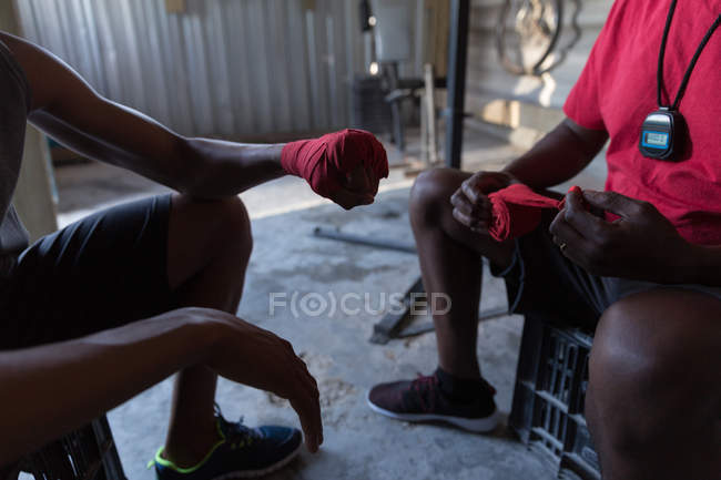 Close-up of trainer assisting male boxer in tying hand wrap on hand — Stock Photo