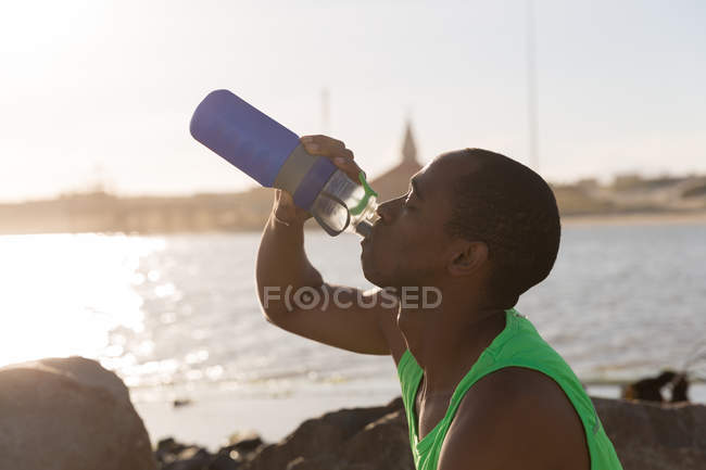Primer plano del atleta masculino bebiendo agua cerca de la playa - foto de stock