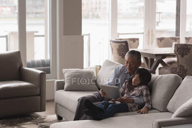 Grandfather and granddaughter using digital tablet on sofa in living room at home — Stock Photo