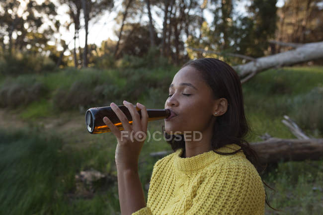 Jovem mulher bebendo cerveja na floresta — Fotografia de Stock