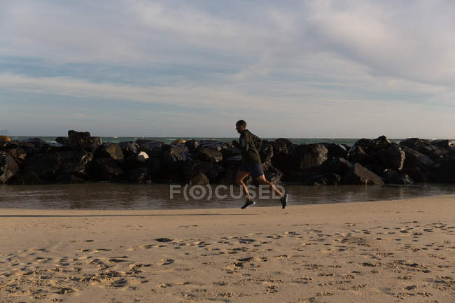 Vista lateral do atleta masculino correndo perto da praia — Fotografia de Stock