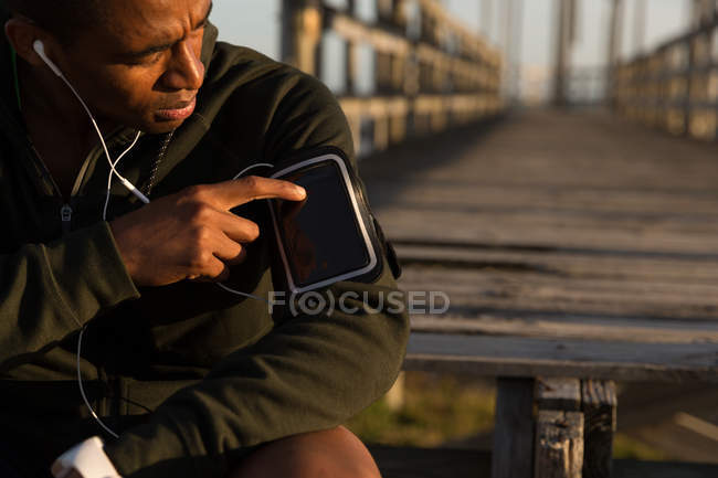 Male athlete using mp3 player on his arm band at beach — Stock Photo