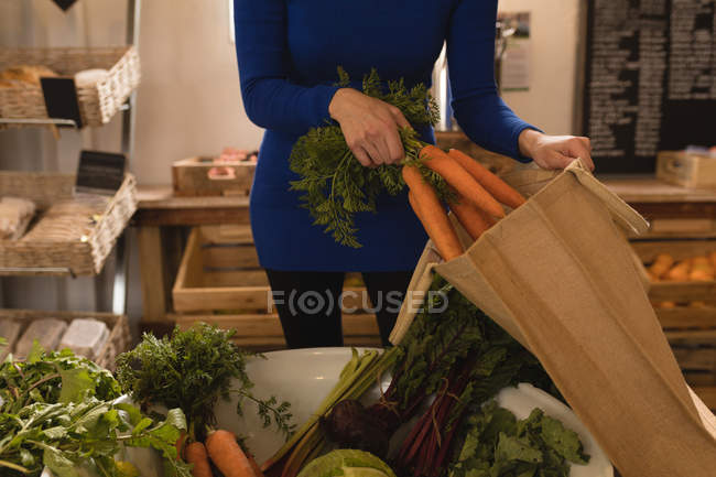 Mid section of woman putting vegetable in shopping bag at supermarket — Stock Photo