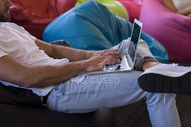 Mid section of business executive using laptop while sitting on bean bag in office — Stock Photo