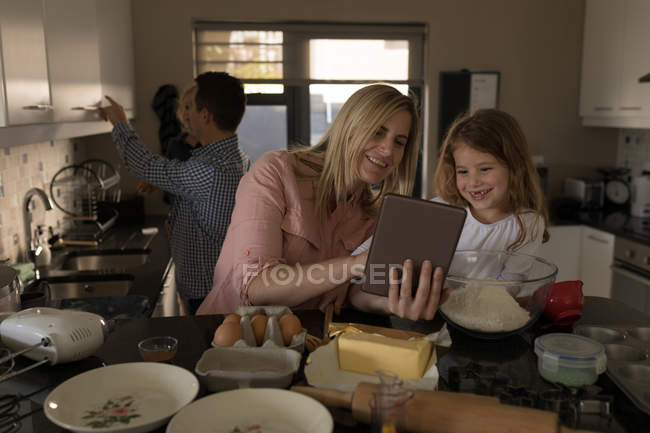 Mujer e hija usando tableta digital en la cocina en casa - foto de stock