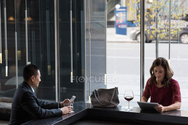 Empresários usando celular e tablet digital em balcão de bar no hotel — Fotografia de Stock