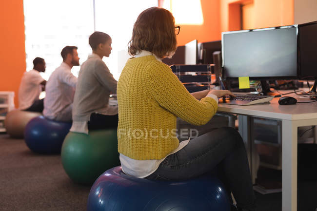 Бизнес-руководители, работающие за столом, сидя на тренировочном мяче в офисе — стоковое фото