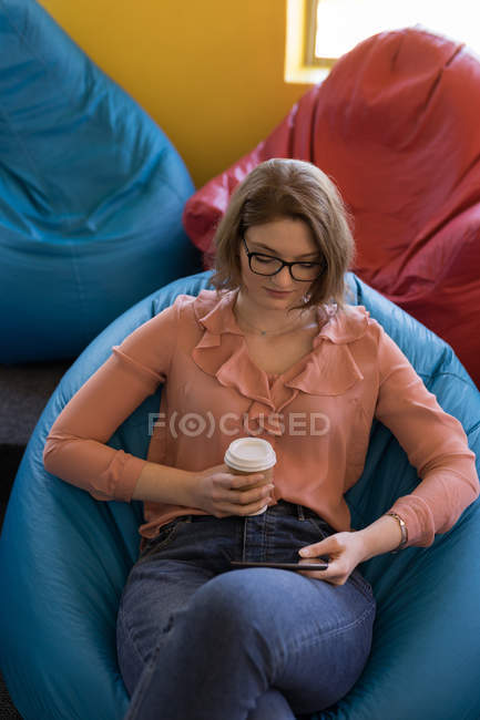 Female business executive using digital tablet while having coffee in office — Stock Photo