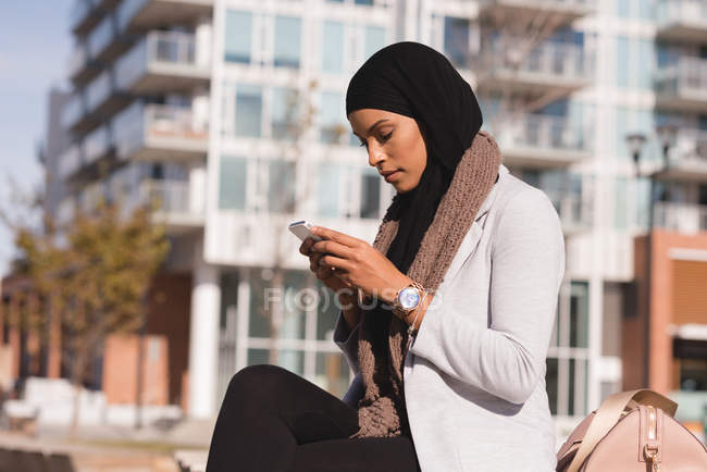 Vista lateral de la mujer hijab utilizando el teléfono móvil en la ciudad - foto de stock