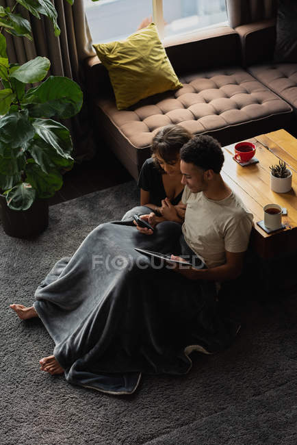 Пара с помощью мобильного телефона и цифрового планшета в гостиной на дому — стоковое фото