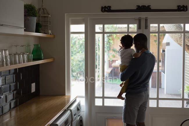 Вид сзади отца и сына, выглядывающих за дверь из кухни — стоковое фото