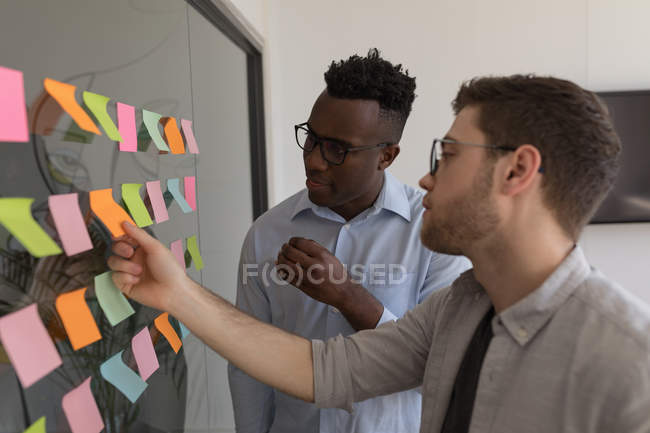 Male executives discussing over sticky notes in office — Stock Photo