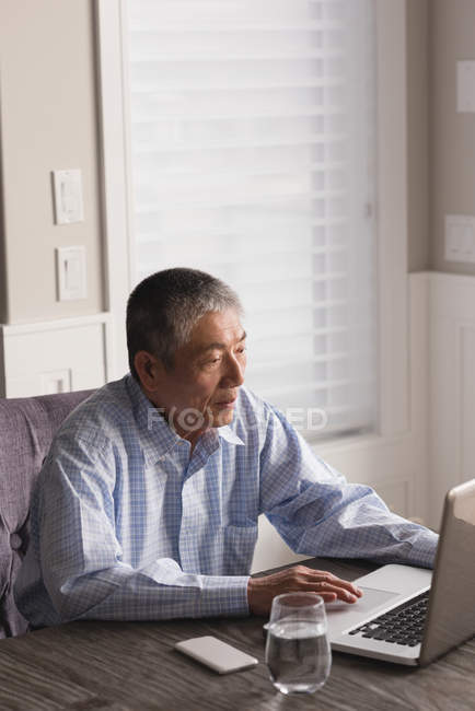 Uomo anziano che utilizza il computer portatile sul tavolo a casa — Foto stock