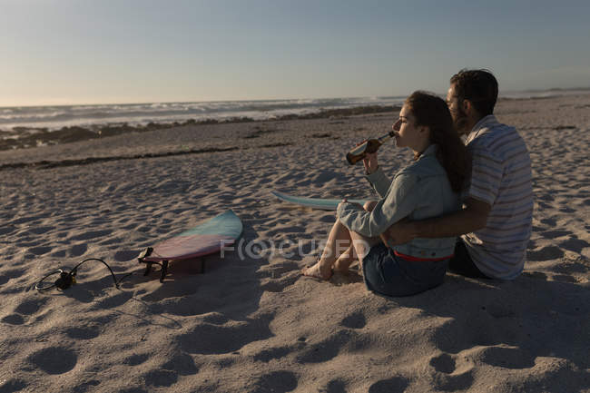 Jovem casal tomando cerveja na praia — Fotografia de Stock